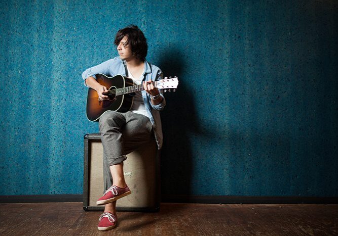 Person playing guitar on amplifier, blue background.