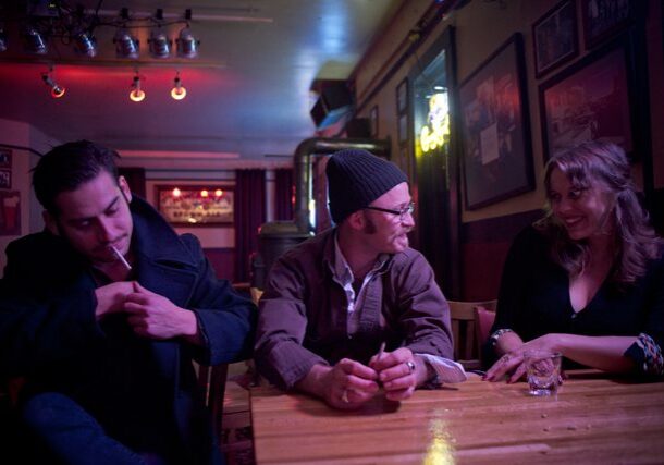 Three people conversing at a dimly lit bar.