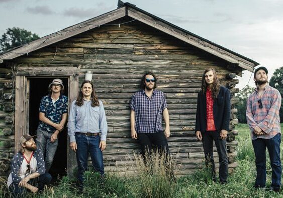 Six people in front of rustic cabin.