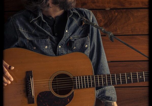 Man holding acoustic guitar, looking sideways.