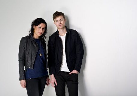 Man and woman standing against white wall.