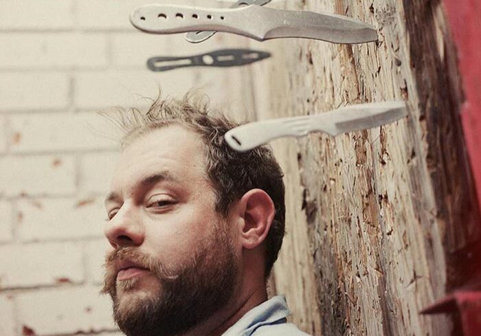 Man with knives stuck in wooden wall.