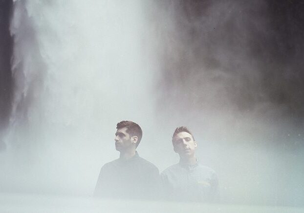 Two men standing near a misty waterfall.