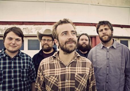Five men standing in plaid shirts outdoors.