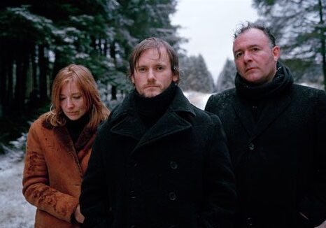 Three people standing in snowy forest.
