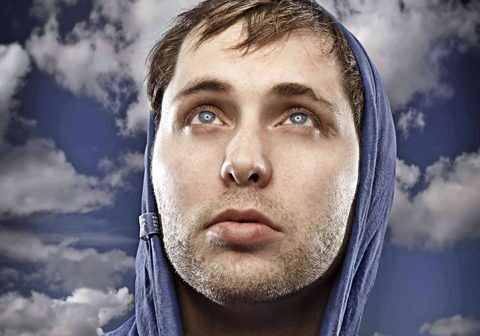Man in hoodie gazing at cloudy sky.