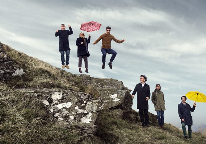 People jumping and walking on grassy hill.