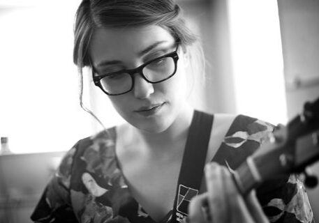 Person playing guitar, wearing glasses, black-and-white.
