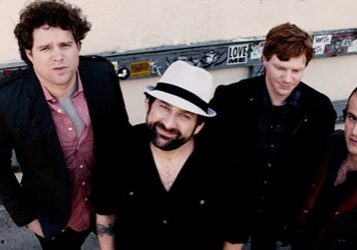 Four men posing outdoors in casual attire.