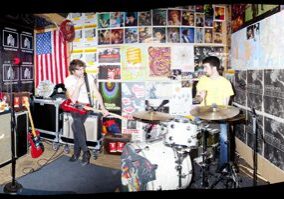 Band rehearsing in a colorful, poster-filled room.