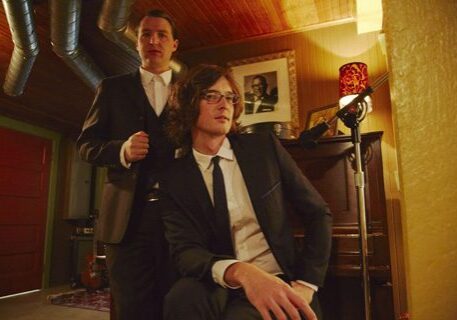Two men in suits by a piano.