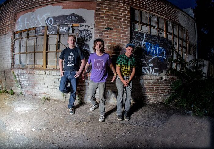 Three people standing by graffiti-covered wall.