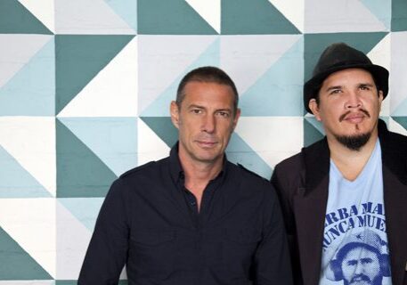 Two men posing against geometric patterned wall.