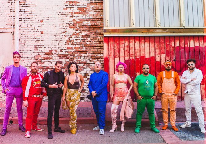 Colorfully dressed group posing against brick wall.