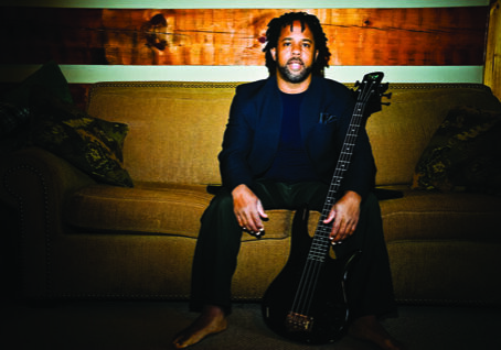 Man sitting on couch with a bass guitar.