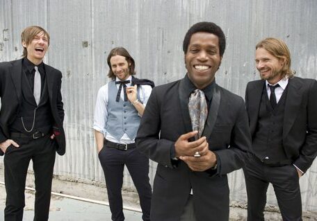 Four men in suits laughing together outdoors.