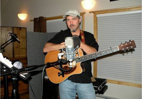 Man playing guitar in a recording studio.