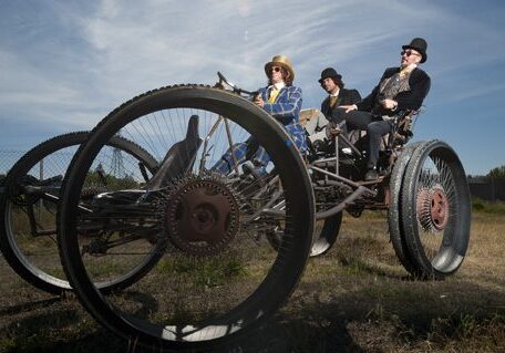 Three people riding a large, vintage tricycle.