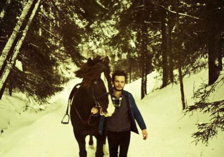 Man walking horse through snowy forest path.