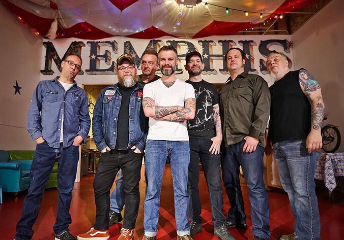 Seven men posing in front of Memphis sign.