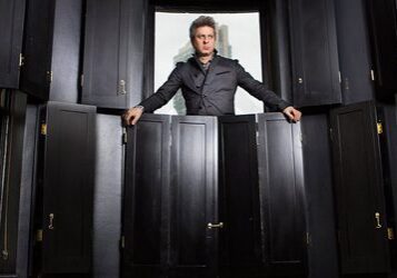 Man standing among black wooden panels.