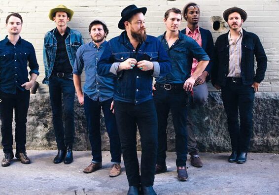 Seven men posing against a brick wall.