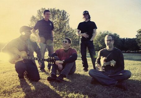 Five men sitting and standing outdoors, relaxed.