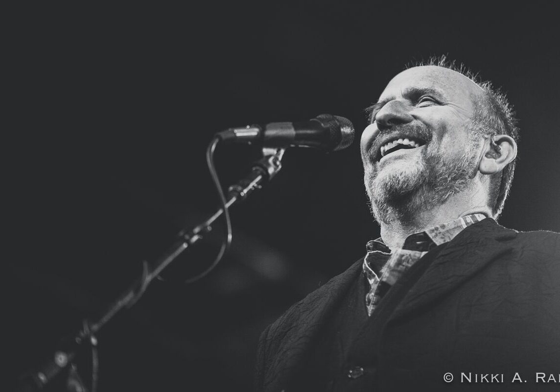 Smiling man singing into a microphone.