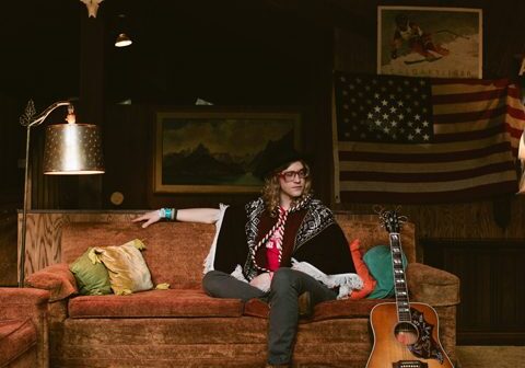 Person sitting on couch with guitar nearby.