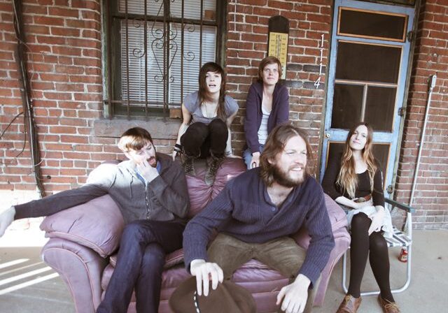Five people sitting on a porch couch.