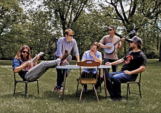 Group of musicians sitting outdoors with instruments.