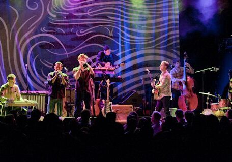 Band performing on stage with colorful backdrop.