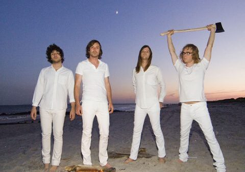 Four people in white by beach bonfire.