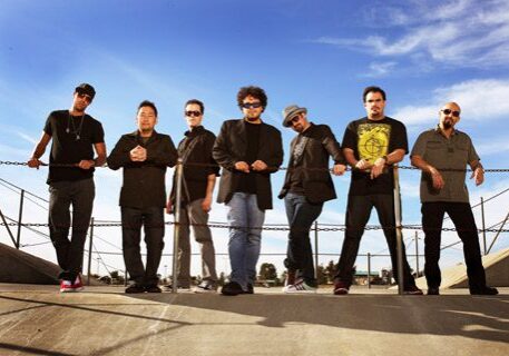 Seven men standing outdoors by railings.
