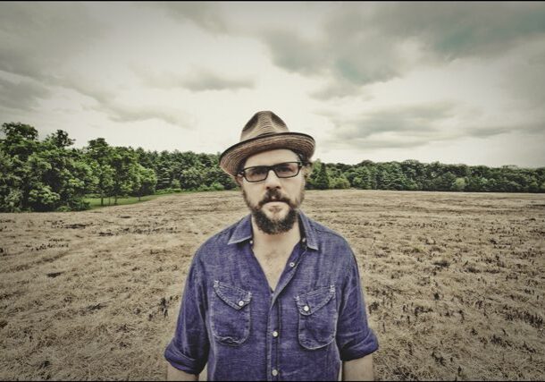 Man in hat standing in dry field.