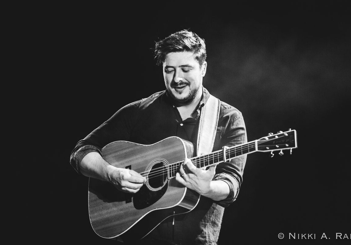 Musician playing acoustic guitar on stage.