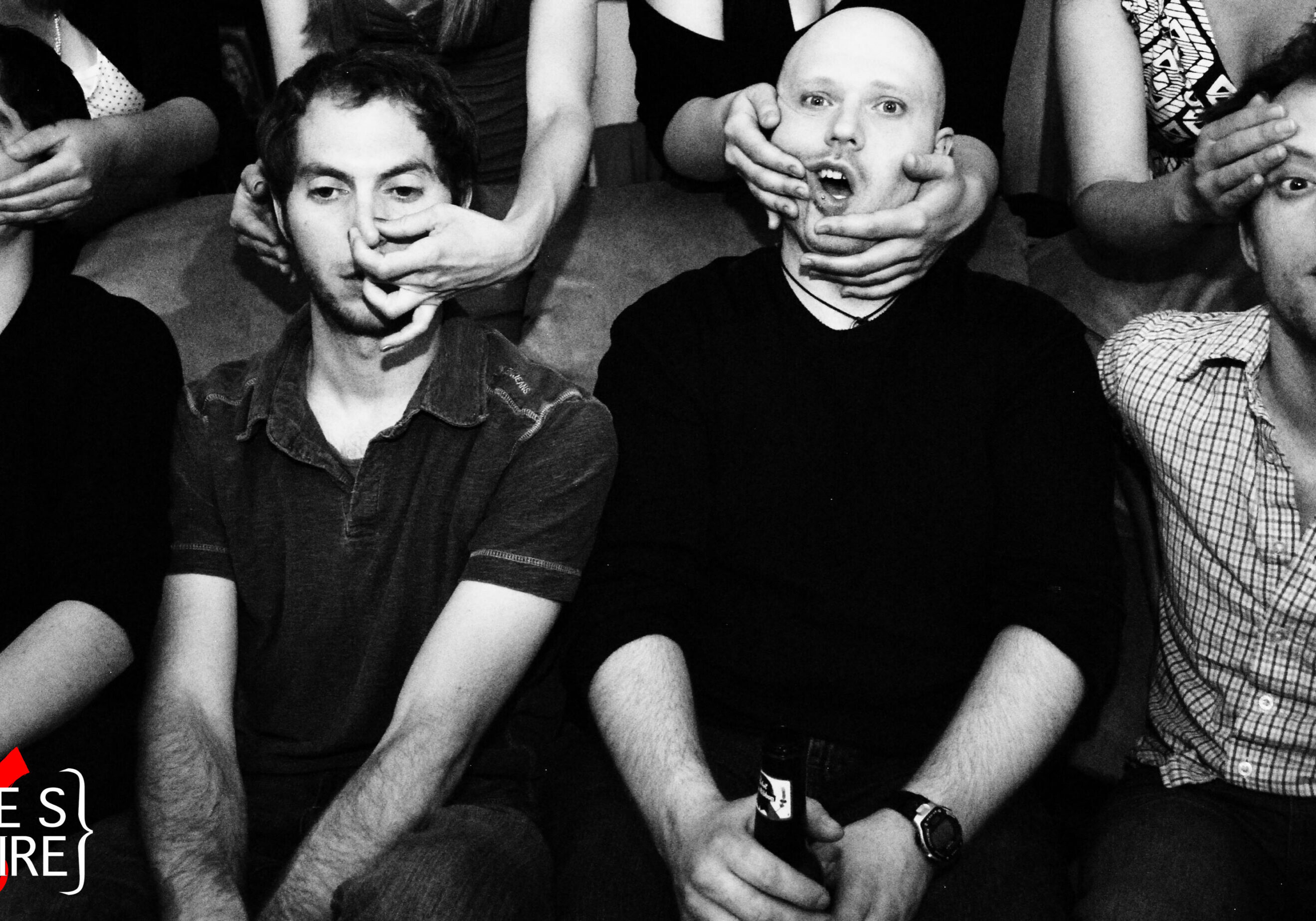 People posing with hands covering faces, smiling.