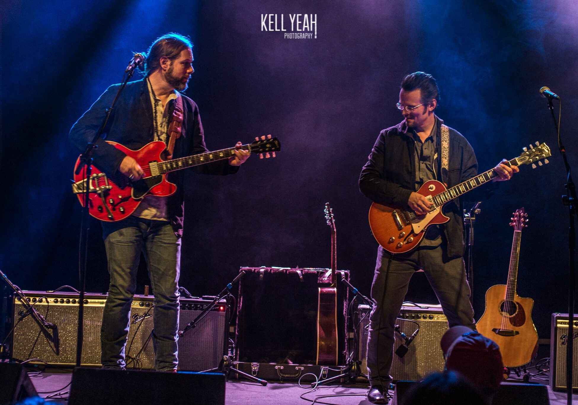 Two musicians playing electric guitars on stage.