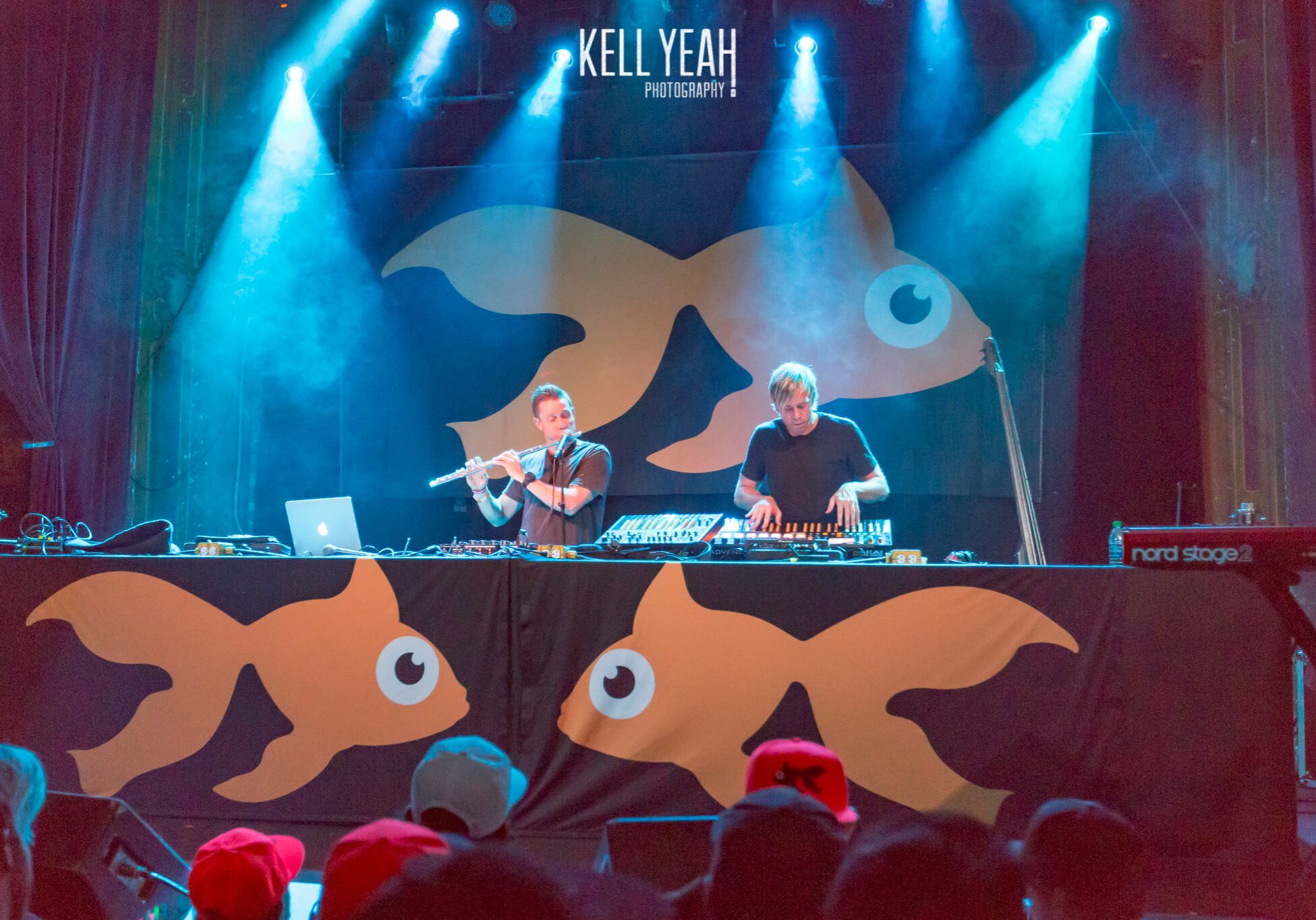 DJs performing on stage with goldfish backdrop.