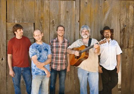 Five men standing with a guitar outdoors.