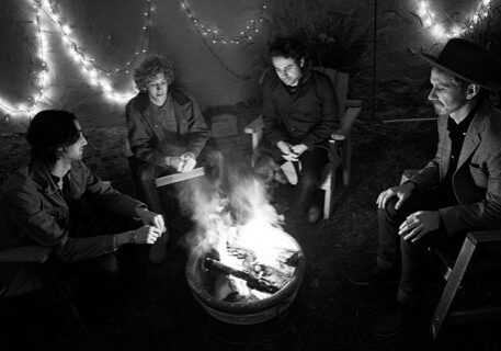 Group sitting around campfire with string lights.