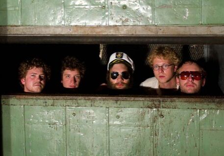 Five men peeking through a metal opening.