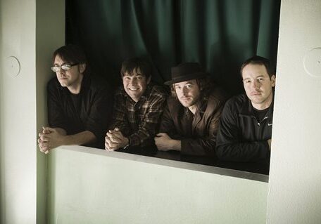 Four men leaning on a green ledge.