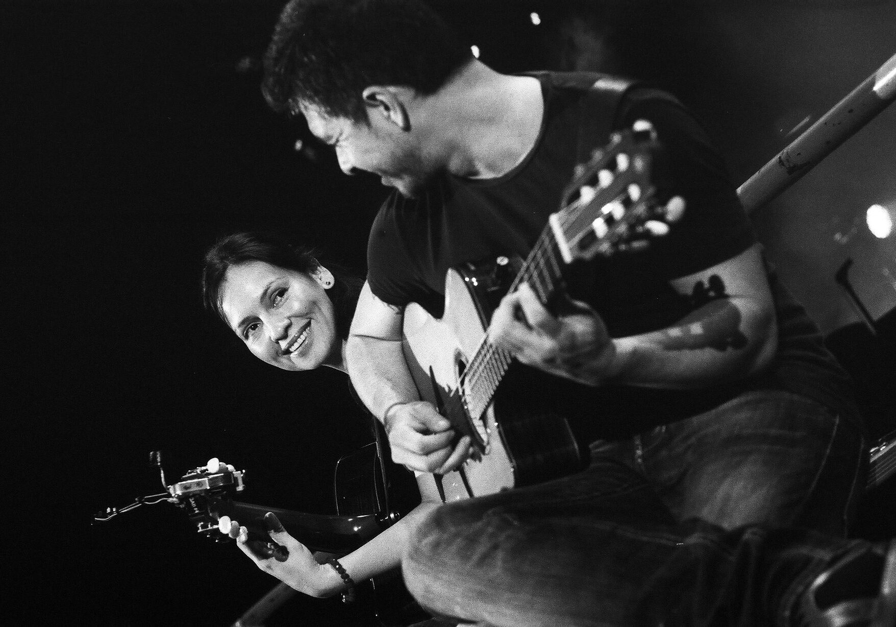 Two people playing guitars, smiling together.