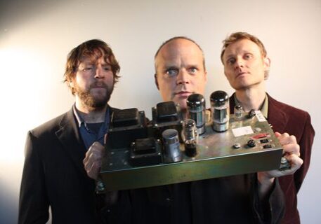 Three men holding a vintage electronic device.