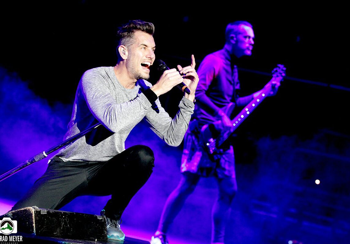 Singer performing energetically on stage with guitarist.