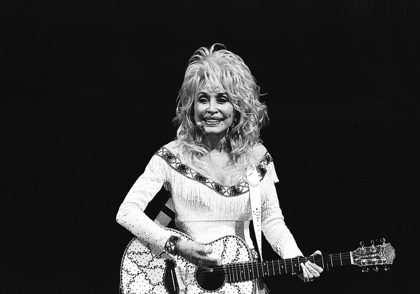 Singer playing guitar on stage, smiling joyfully.