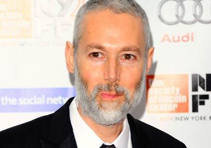 Man with gray beard at event backdrop.