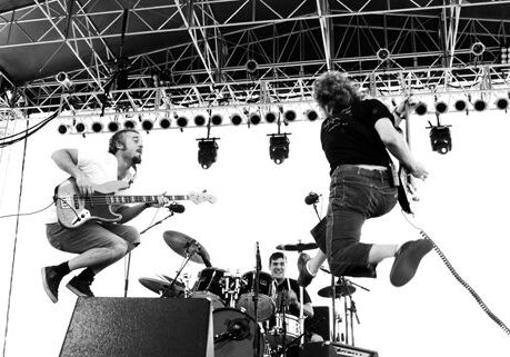 Band performing energetically on stage, musicians jumping.