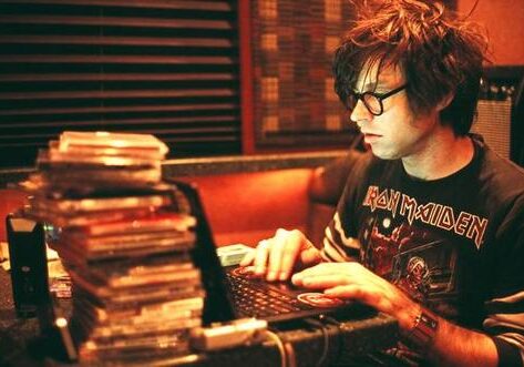 Person typing on laptop near CD stack.